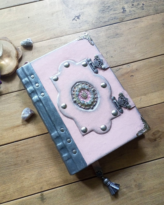 A pink hardcover journal with ornate silver metal corner and center embellishments, brooch with crystals