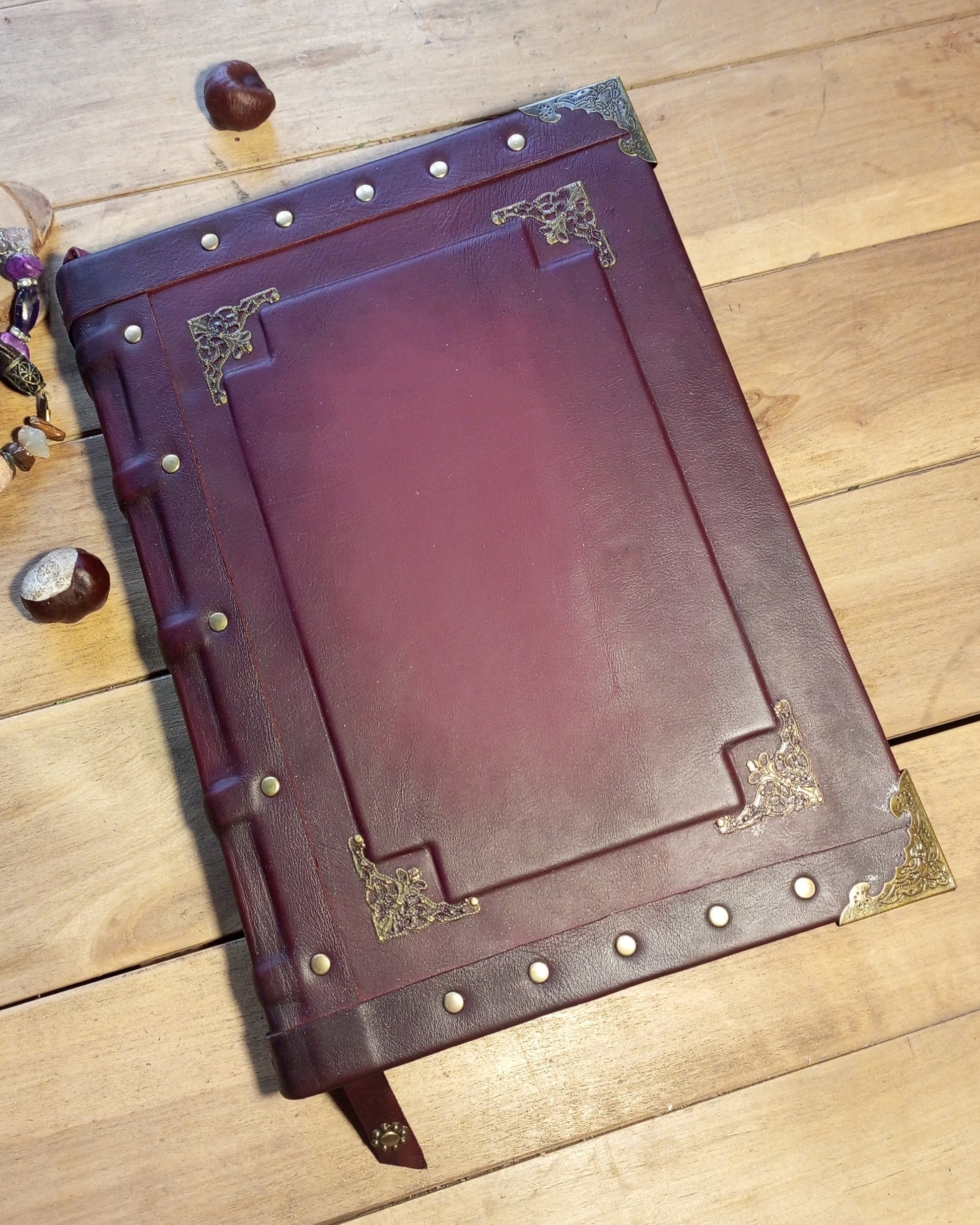 Aged bordeaux leather-bound journal with brass accents on a wooden surface