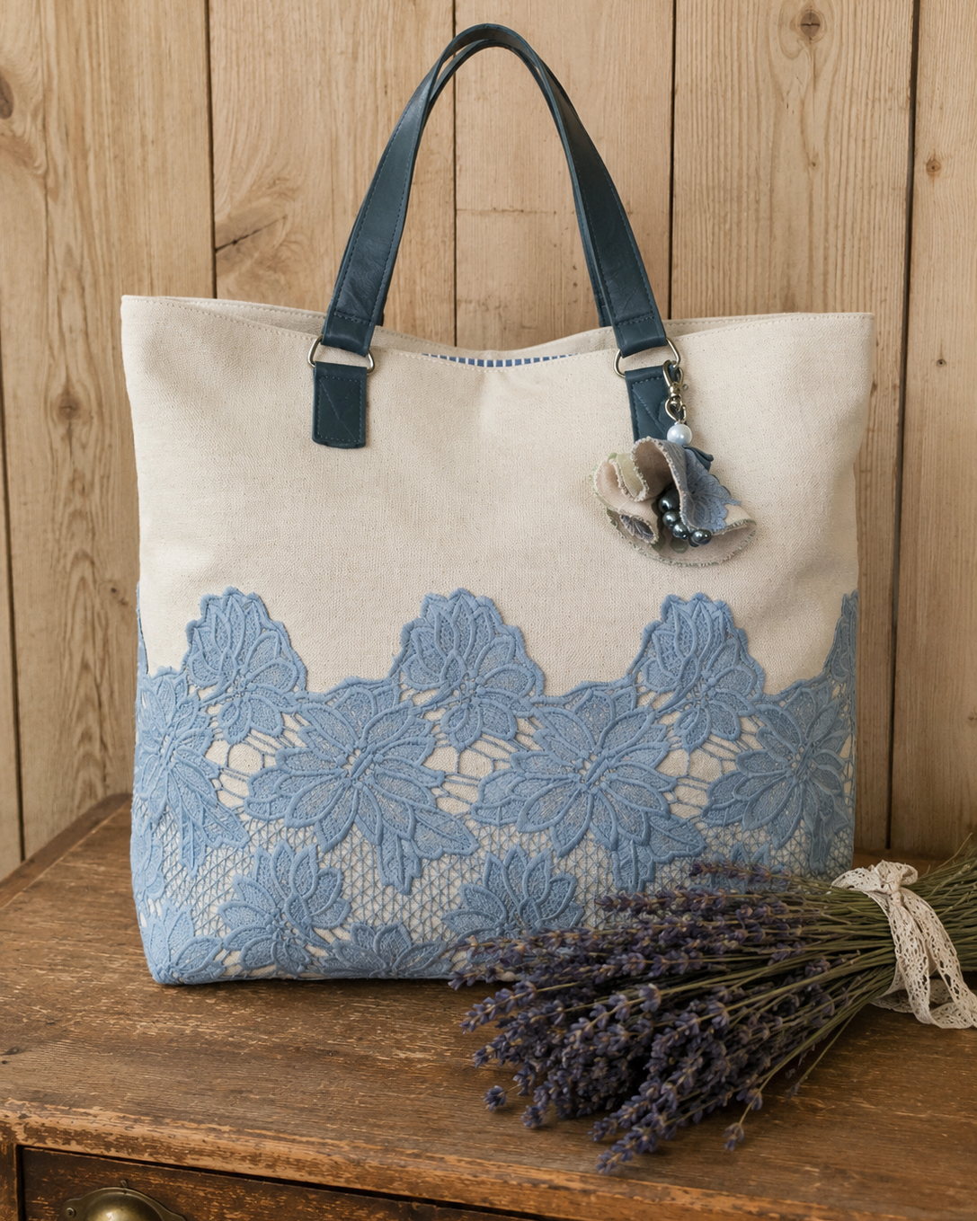 Beige tote bag with blue floral lace design on a wooden surface with lavender.