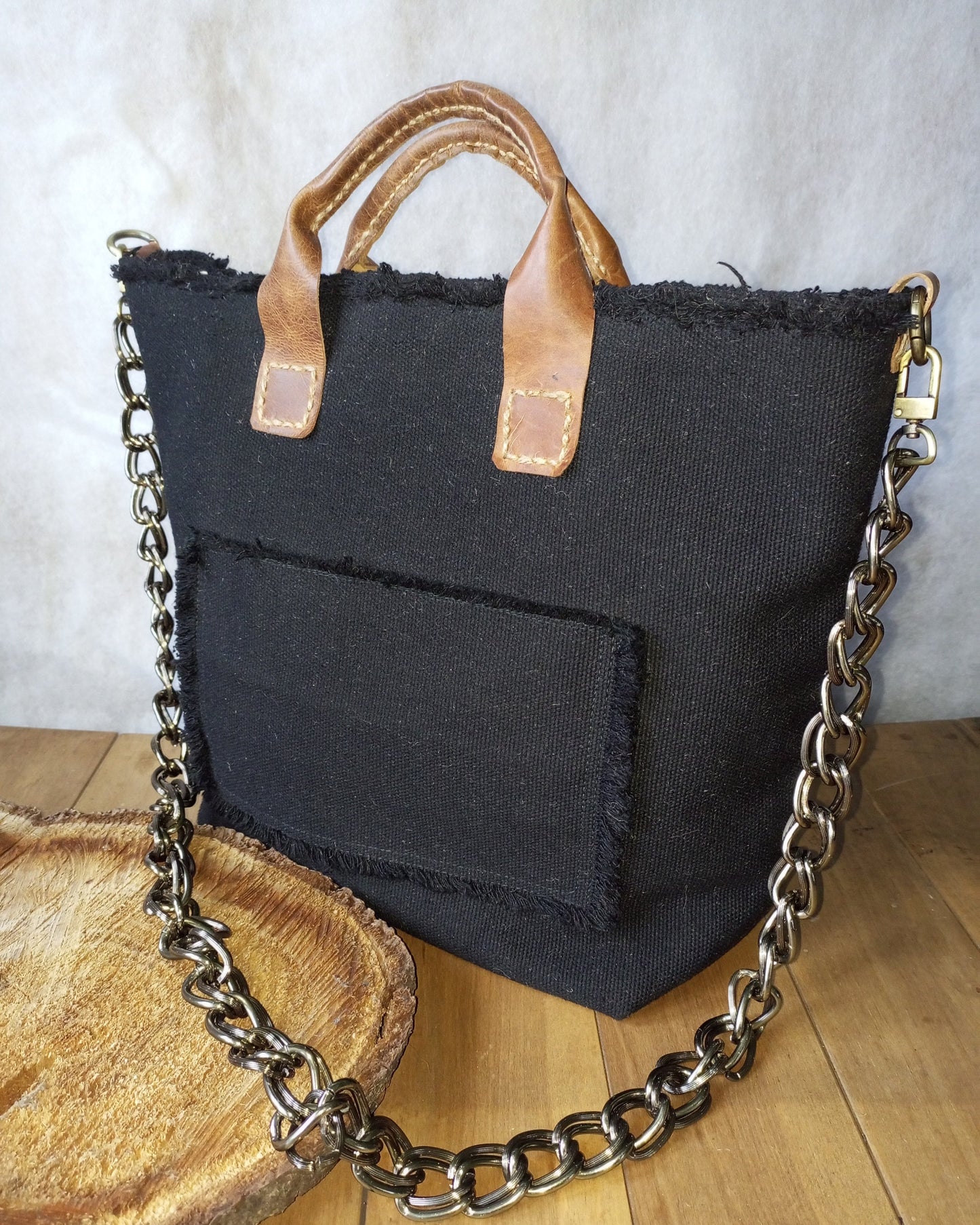Black canvas tote bag with leather handles and chain detail on a wooden surface.