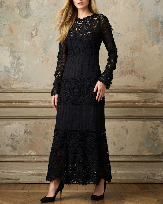 Woman wearing a crochet maxi black lace dress with long sleeves standing against an ornate wall.