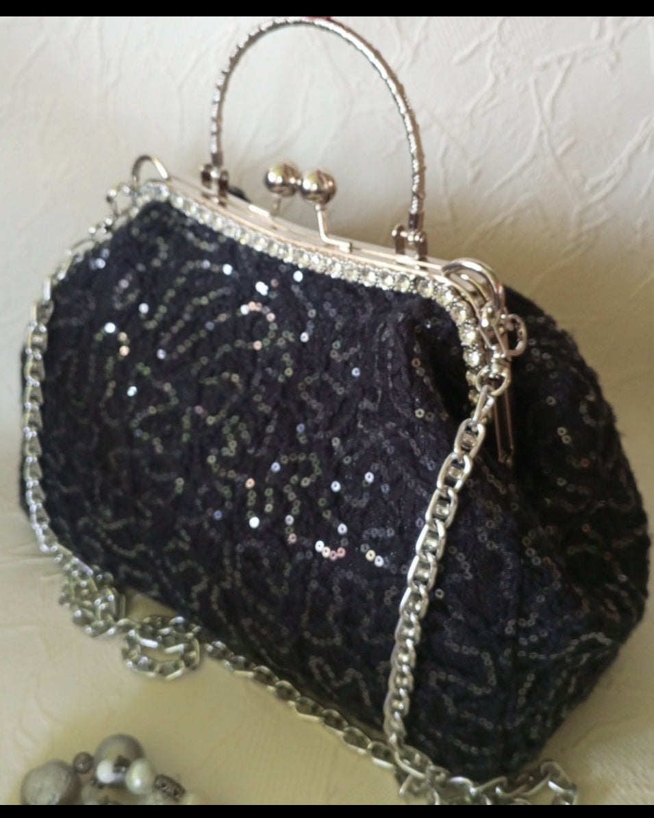 Black sequined handbag with silver frame and chain strap on a textured white background
