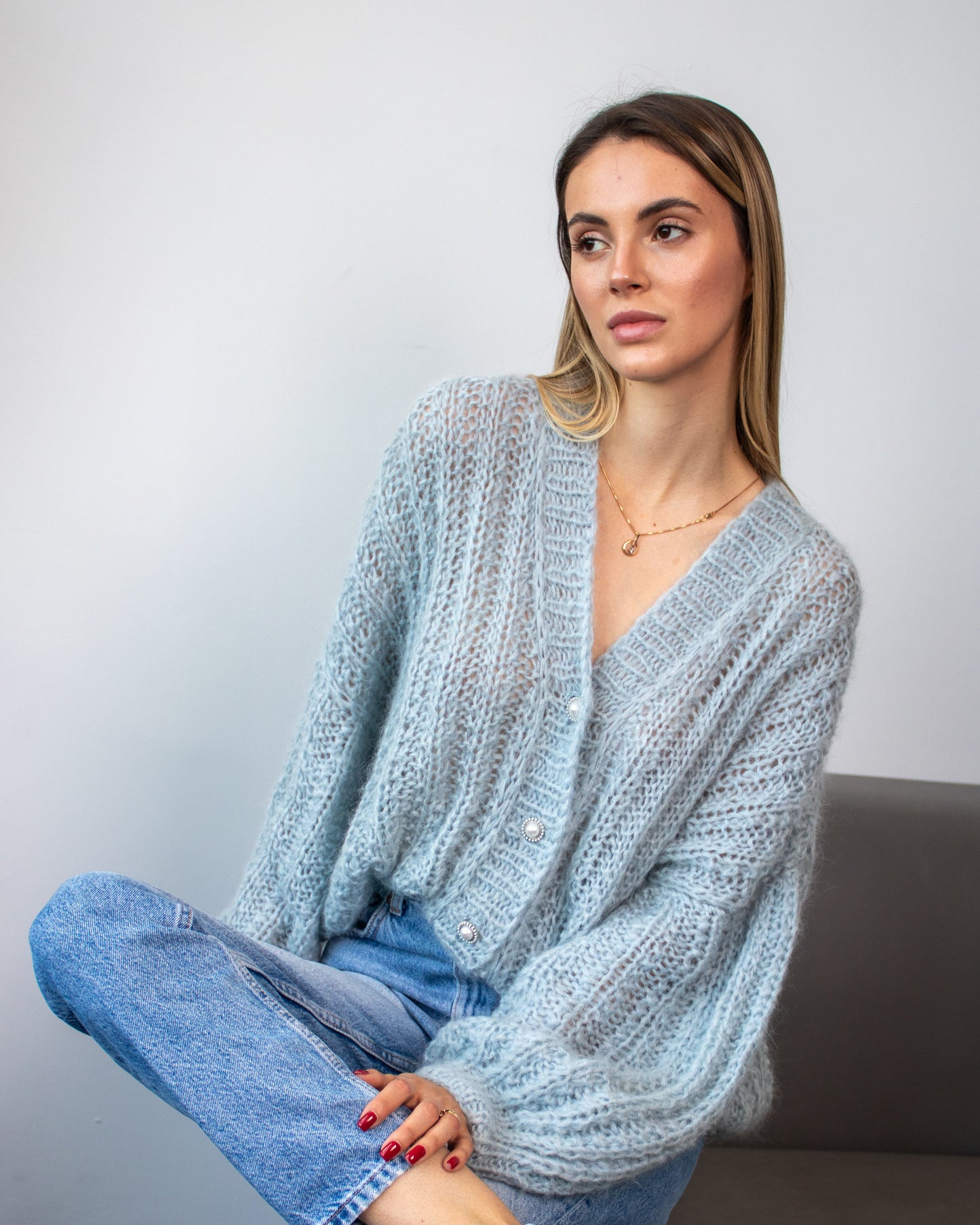 Woman wearing a light blue knitted cardigan and jeans sitting on a couch.