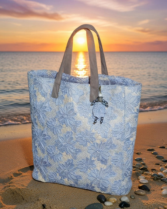 Blue floral guipure lace tote bag with leather handles on a beach with sunset in the background