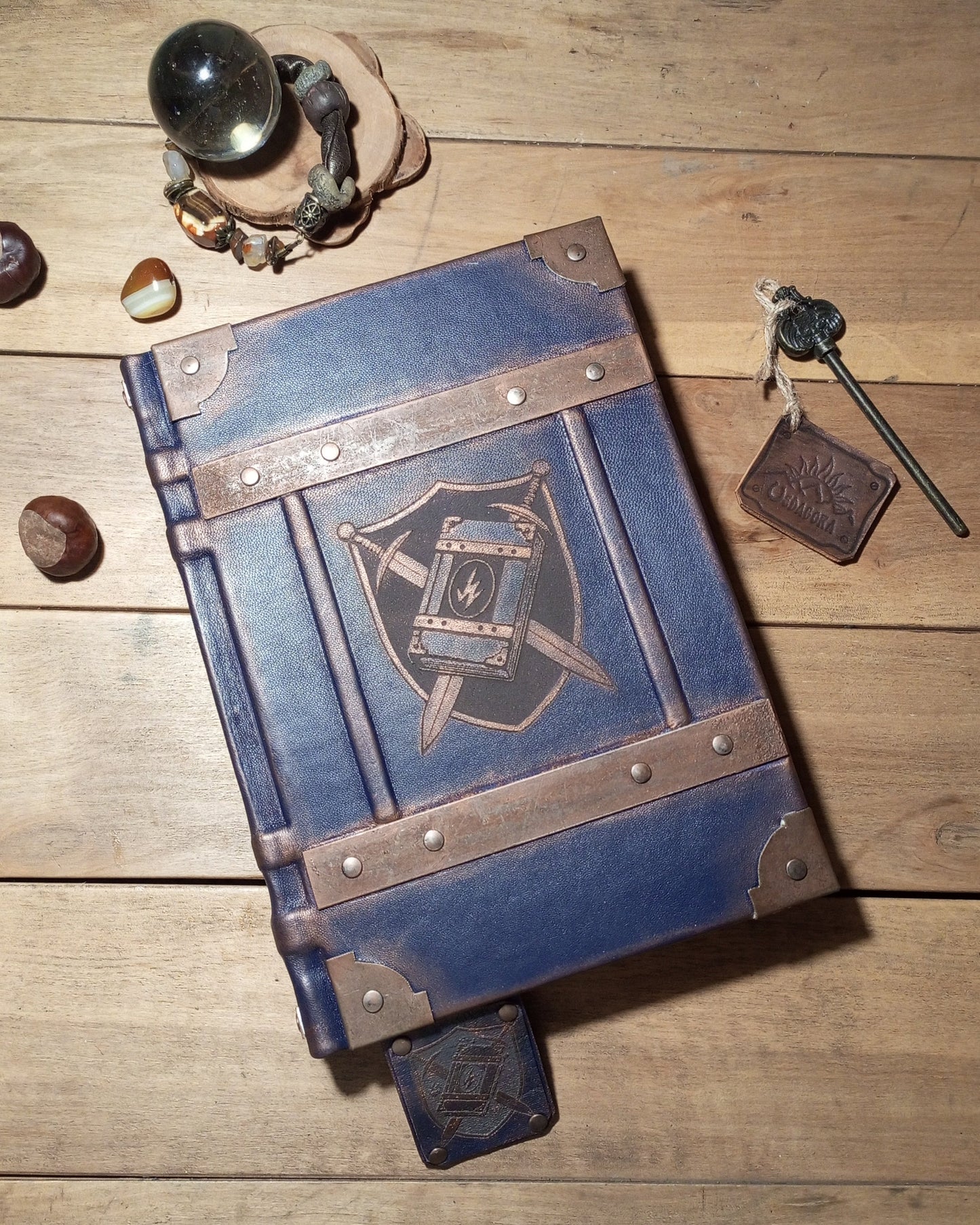 Blue leather-bound book with metallic accents on a wooden surface, surrounded by fantasy-themed items.