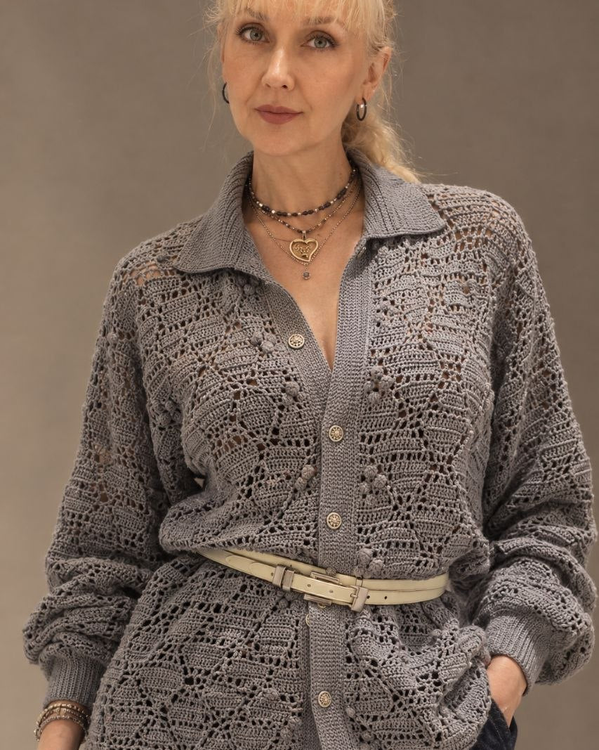 A woman wearing a gray open-knit button-up shirt with a collar, styled with a light grey belt
