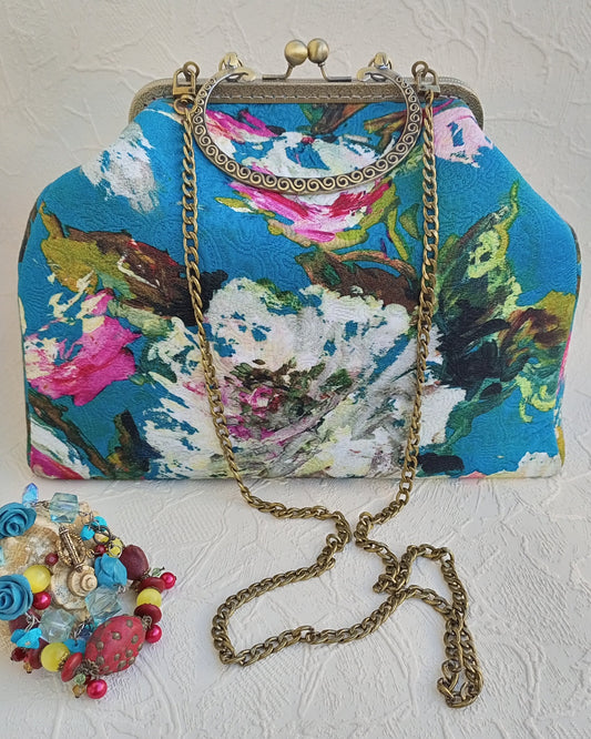 Floral patterned kisslock handbag with a chain strap on a textured white background