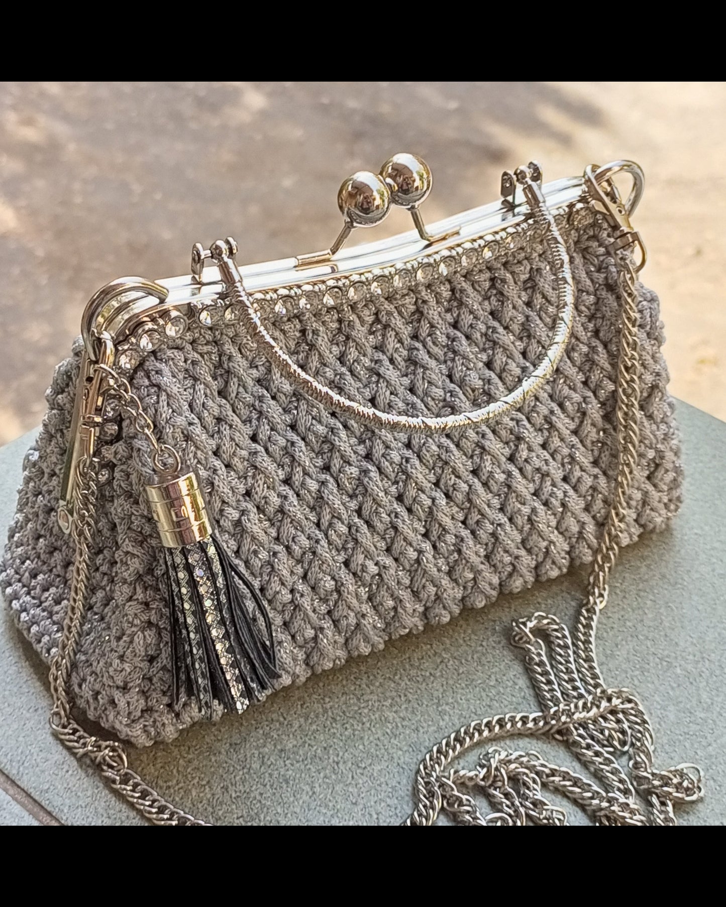 Gray crochet handbag with a chain strap kisslock clasp and leather tassel 