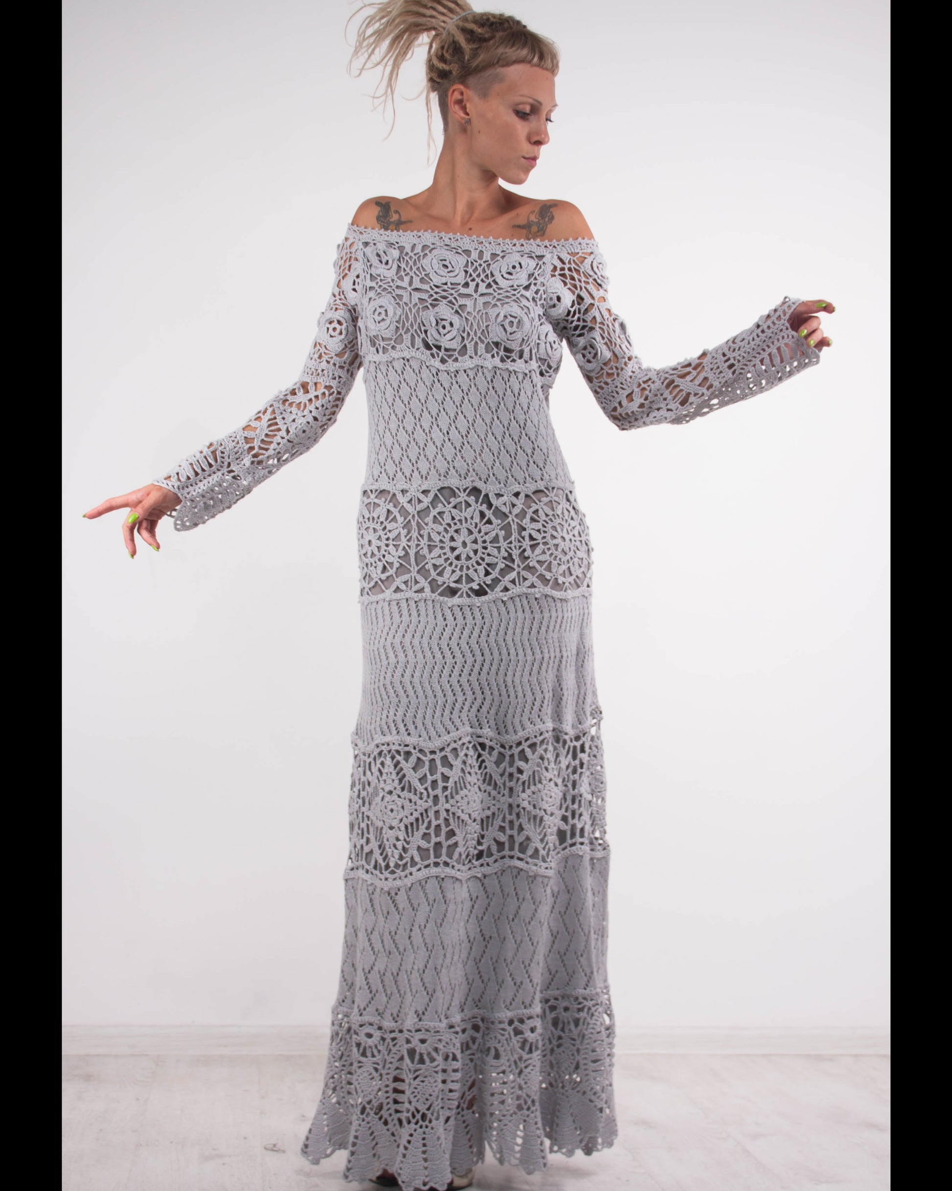 Woman wearing a long, grey off-shoulder crochet dress on a white background
