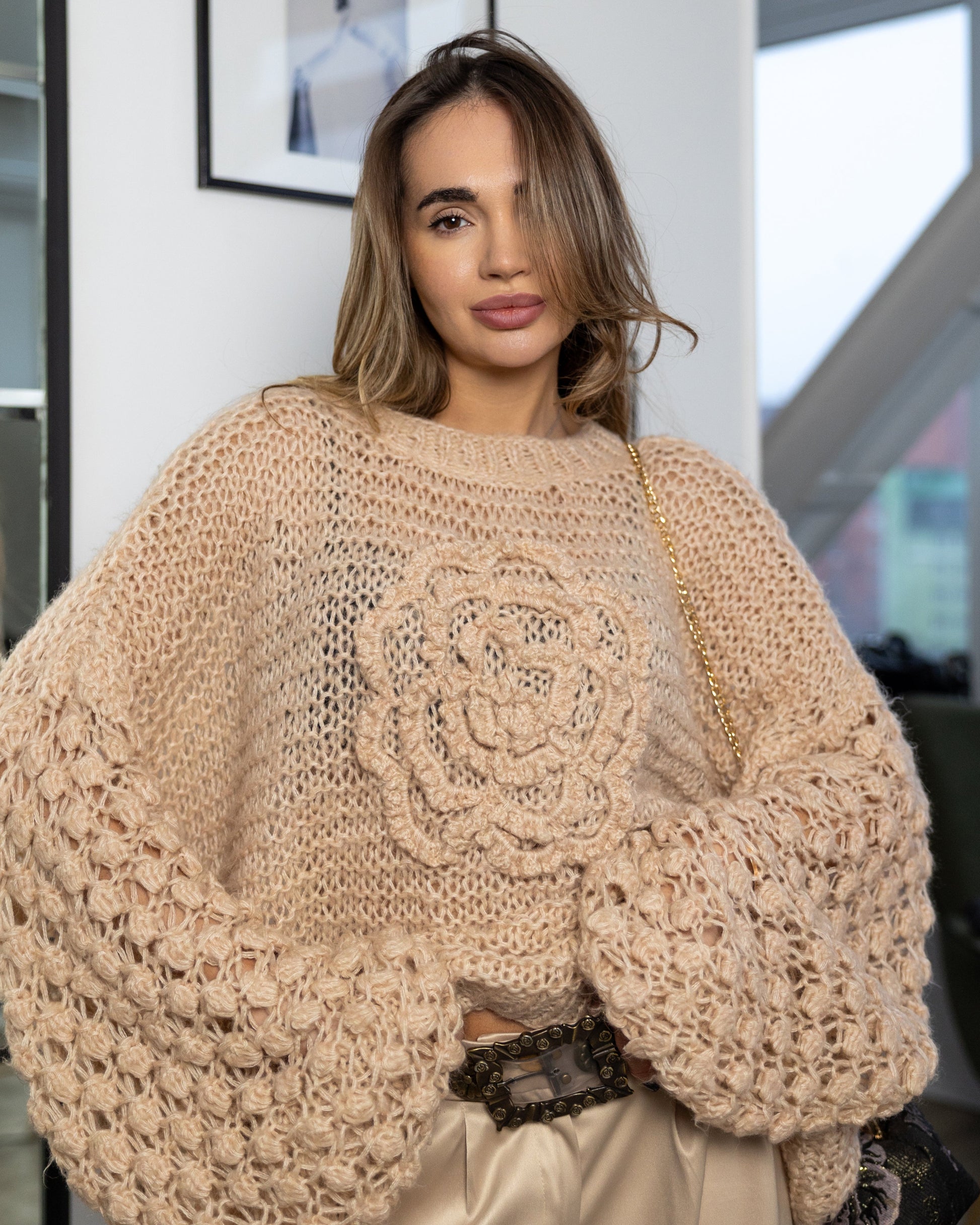Woman wearing a beige knit sweater with a floral pattern in an indoor setting.