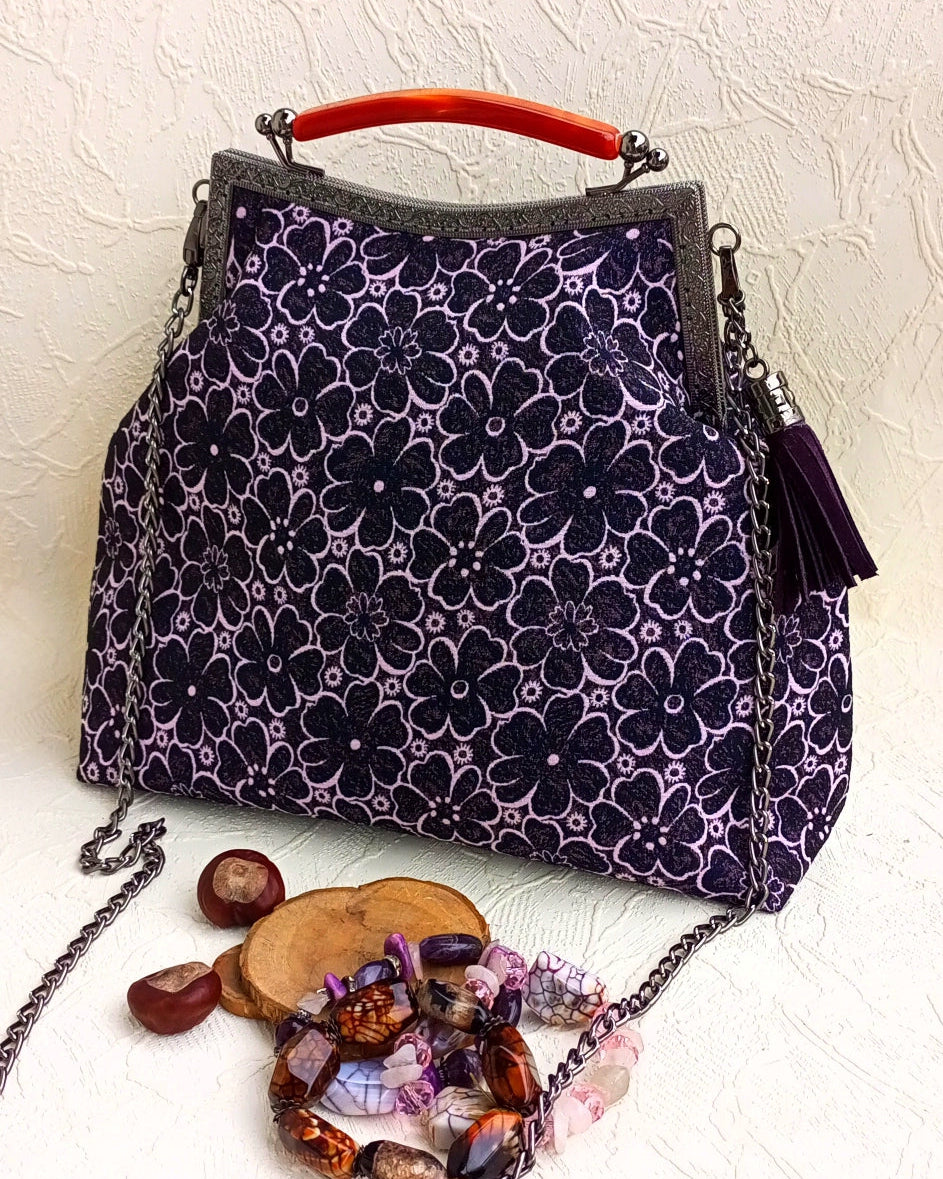 Purple floral patterned handbag with a red handle and silver isslock clasp and removable silver chain