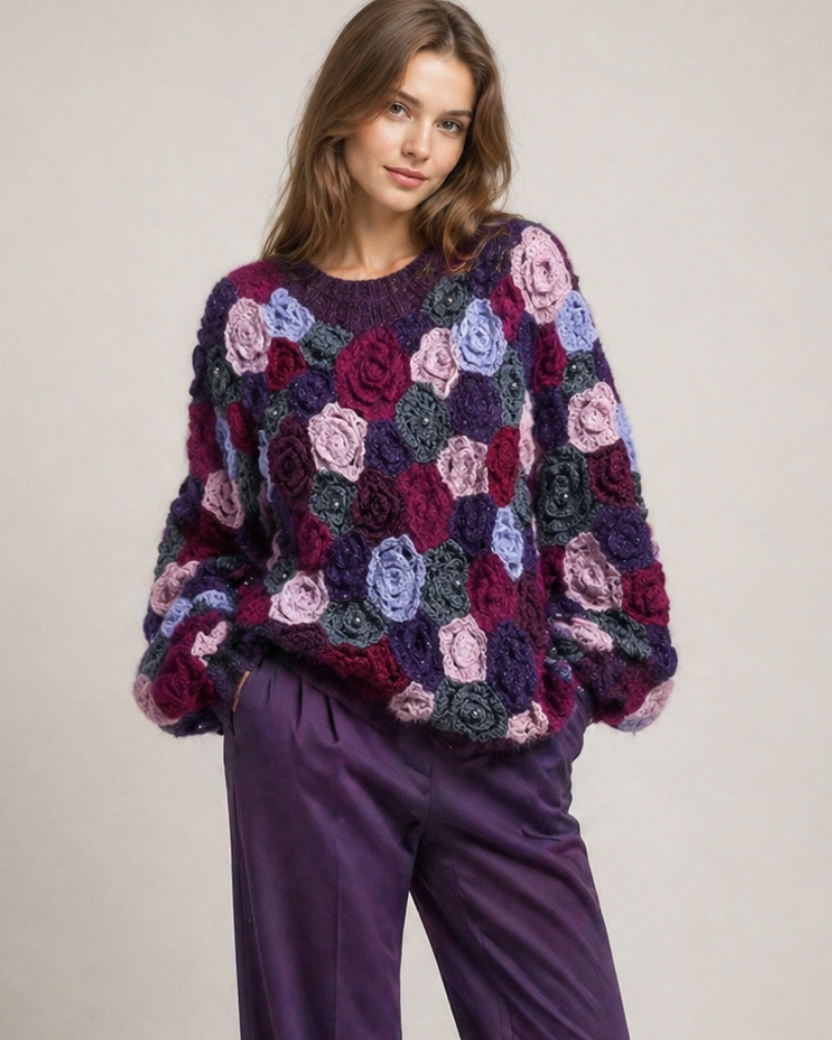 Woman wearing a colorful floral crochet irish lace sweater and purple pants on a plain background