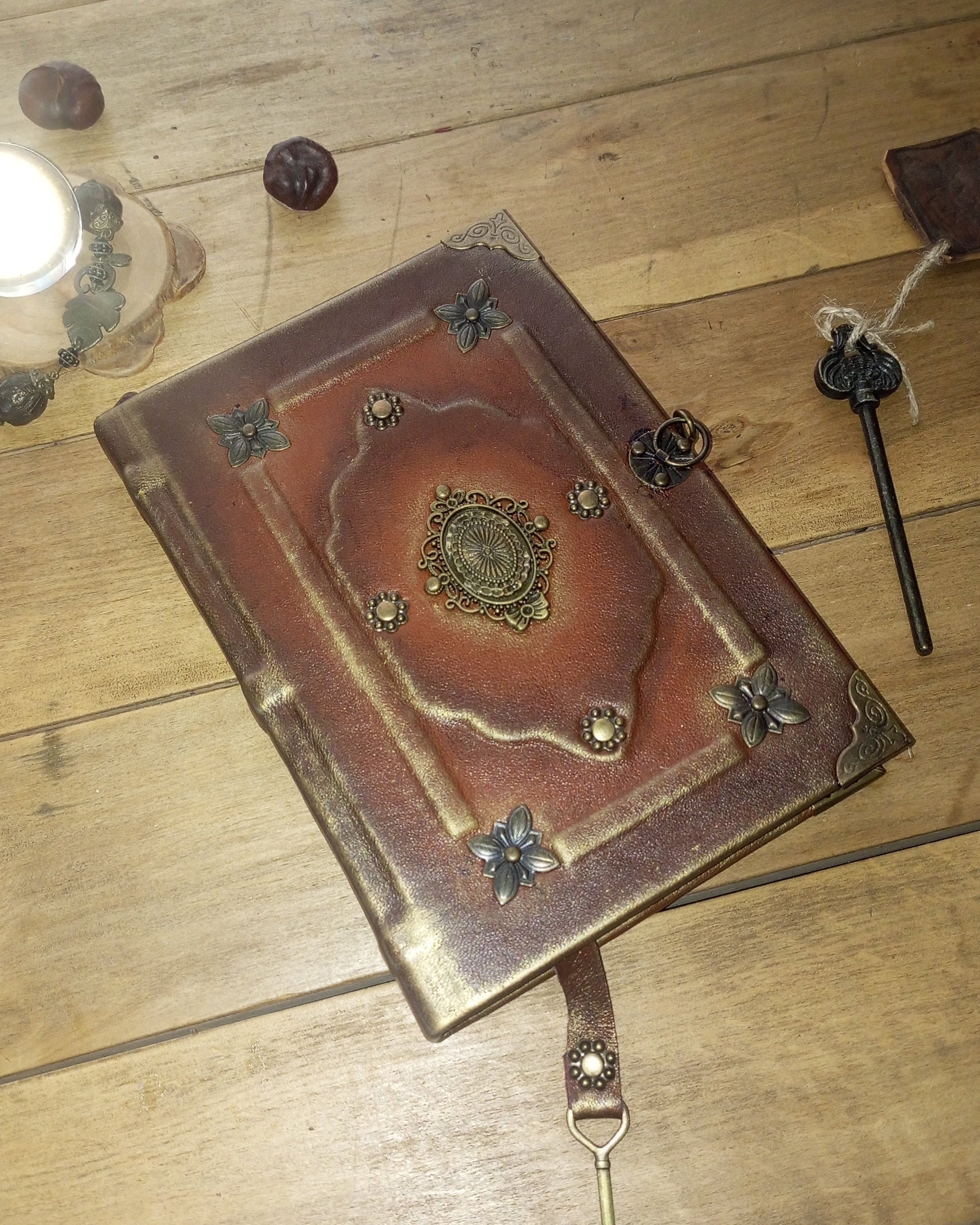 A decorative brown leather-bound journal or notebook with ornate metal corner and center embellishments, shown on a wooden tabletop 