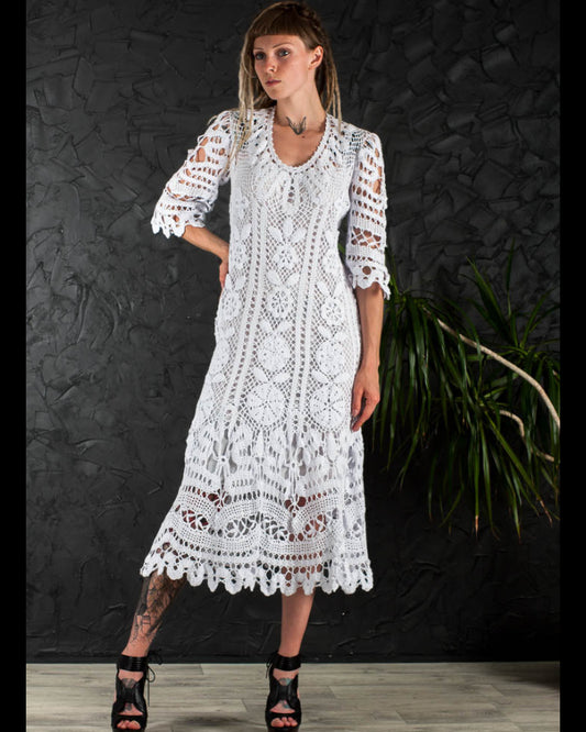 Woman wearing a crochet irish lace white boho wedding dress against a dark textured wall.
