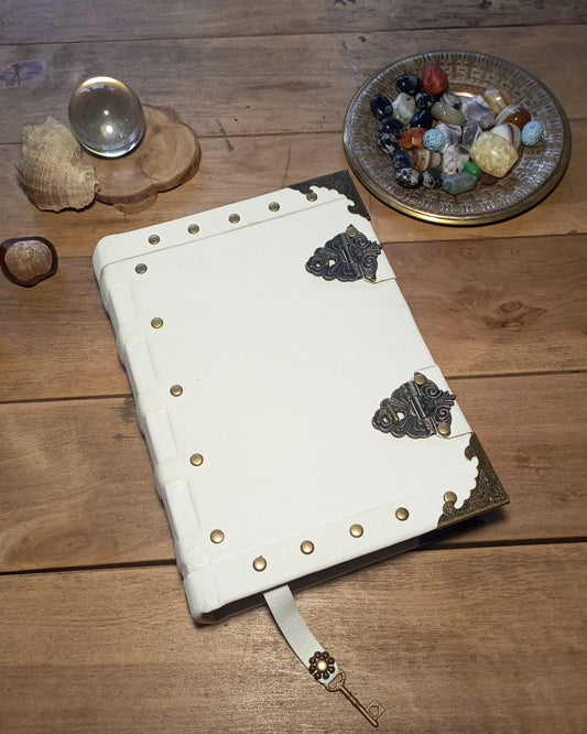 White leather notebook with metal clasps on a wooden surface with crystals and stones.